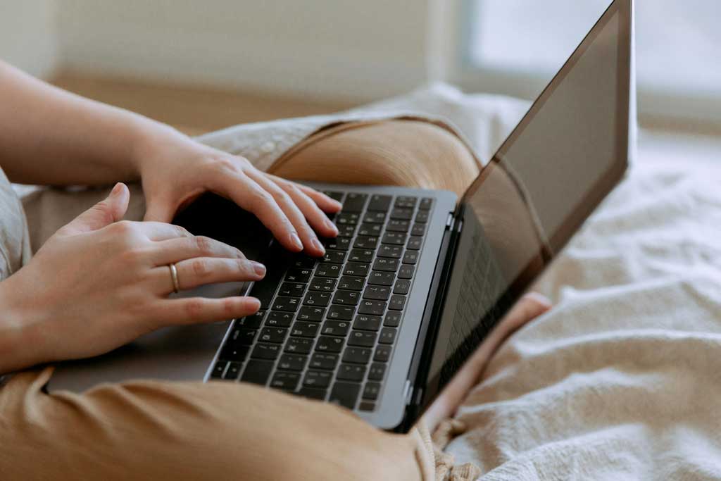 Woman using laptop while sitting on bed