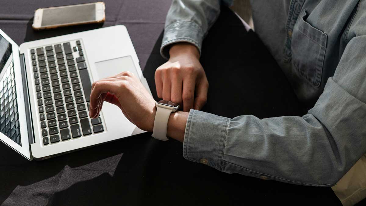Person checking Apple Watch on desk with Mac Book Air