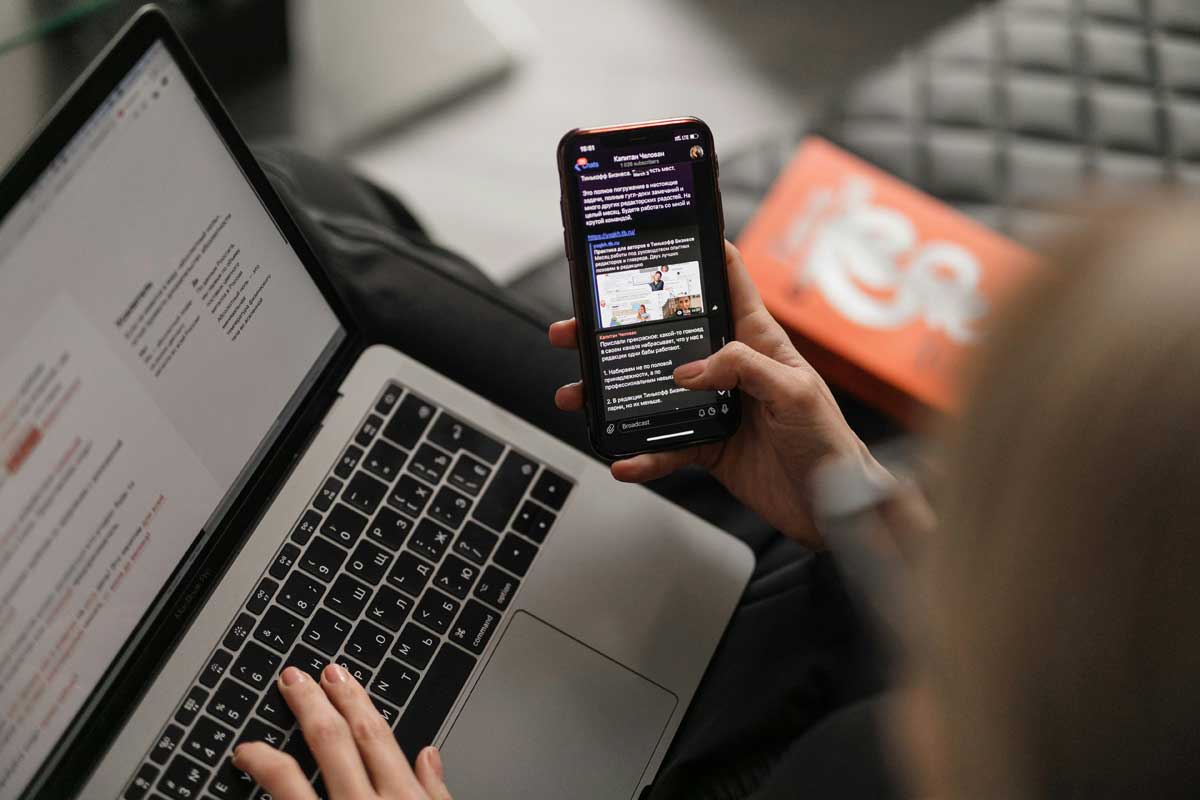 Young woman on leather couch working at a laptop while browsing her phone
