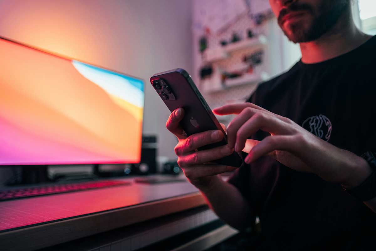 Young man holding an iPhone 12 Pro Max in front of his desk.