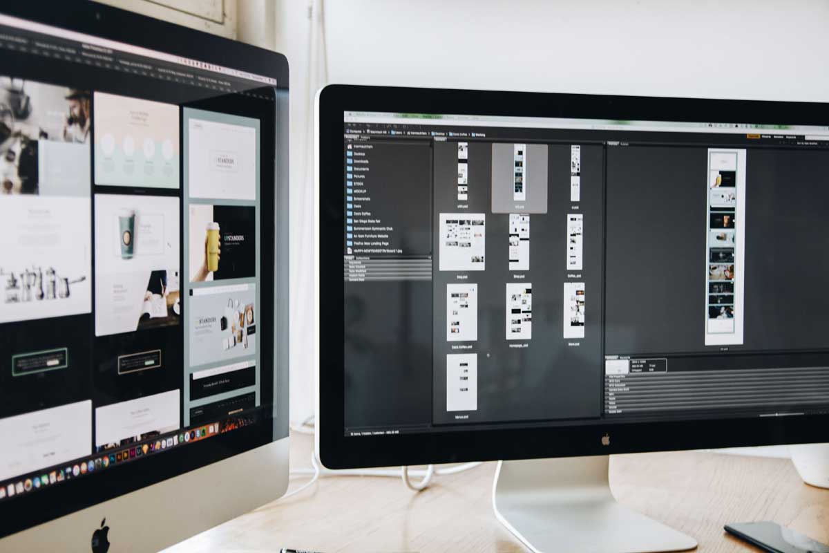 A modern workspace featuring dual computer monitors displaying web design projects