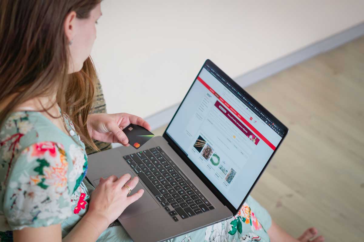Woman in floral dress shopping online with a laptop and credit card indoors