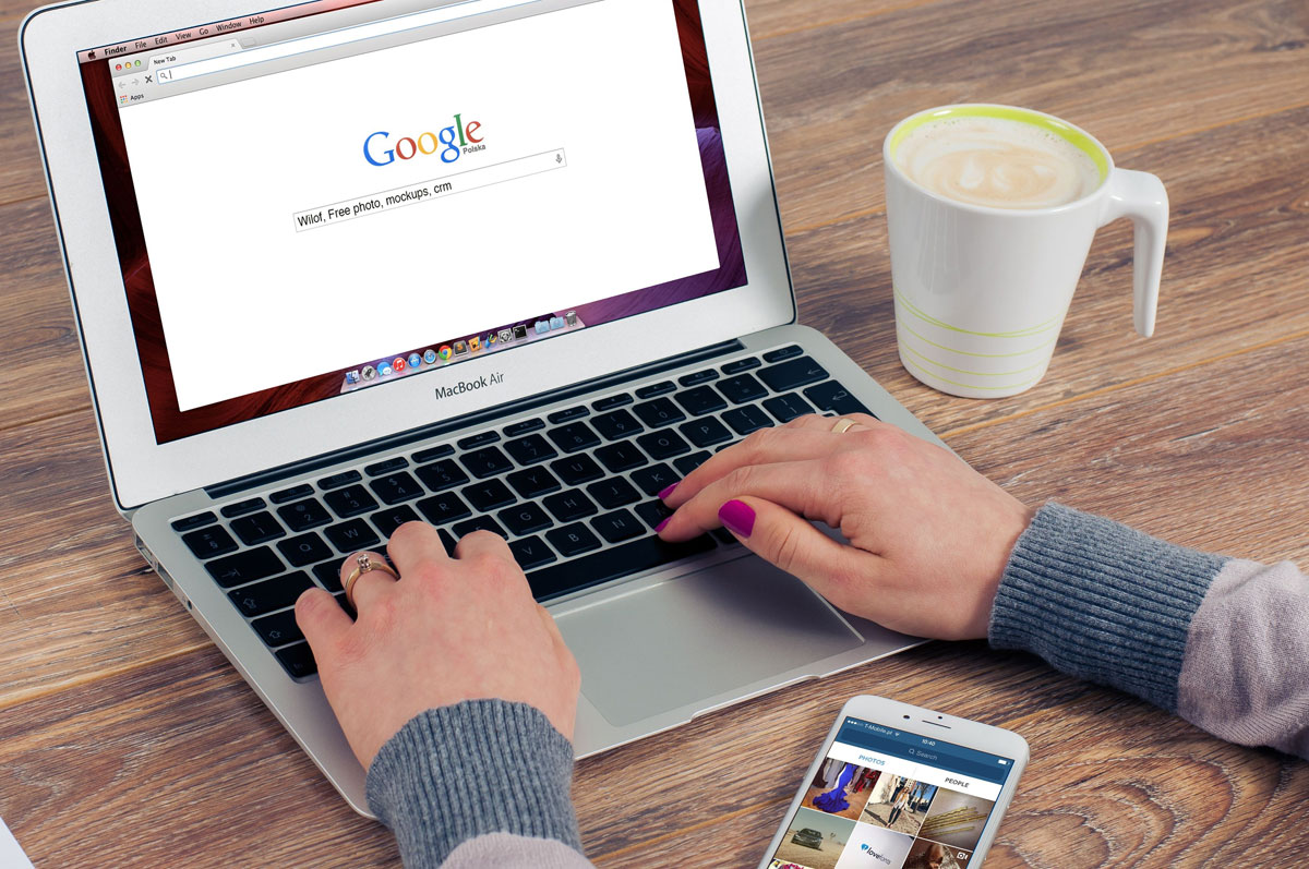 Hands typing on MacBook Air with Google search open, coffee nearby