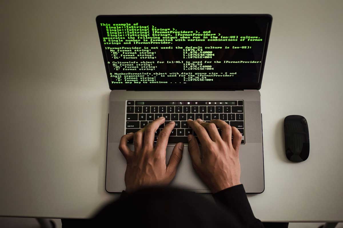 Hands typing code on a laptop with programming text on screen