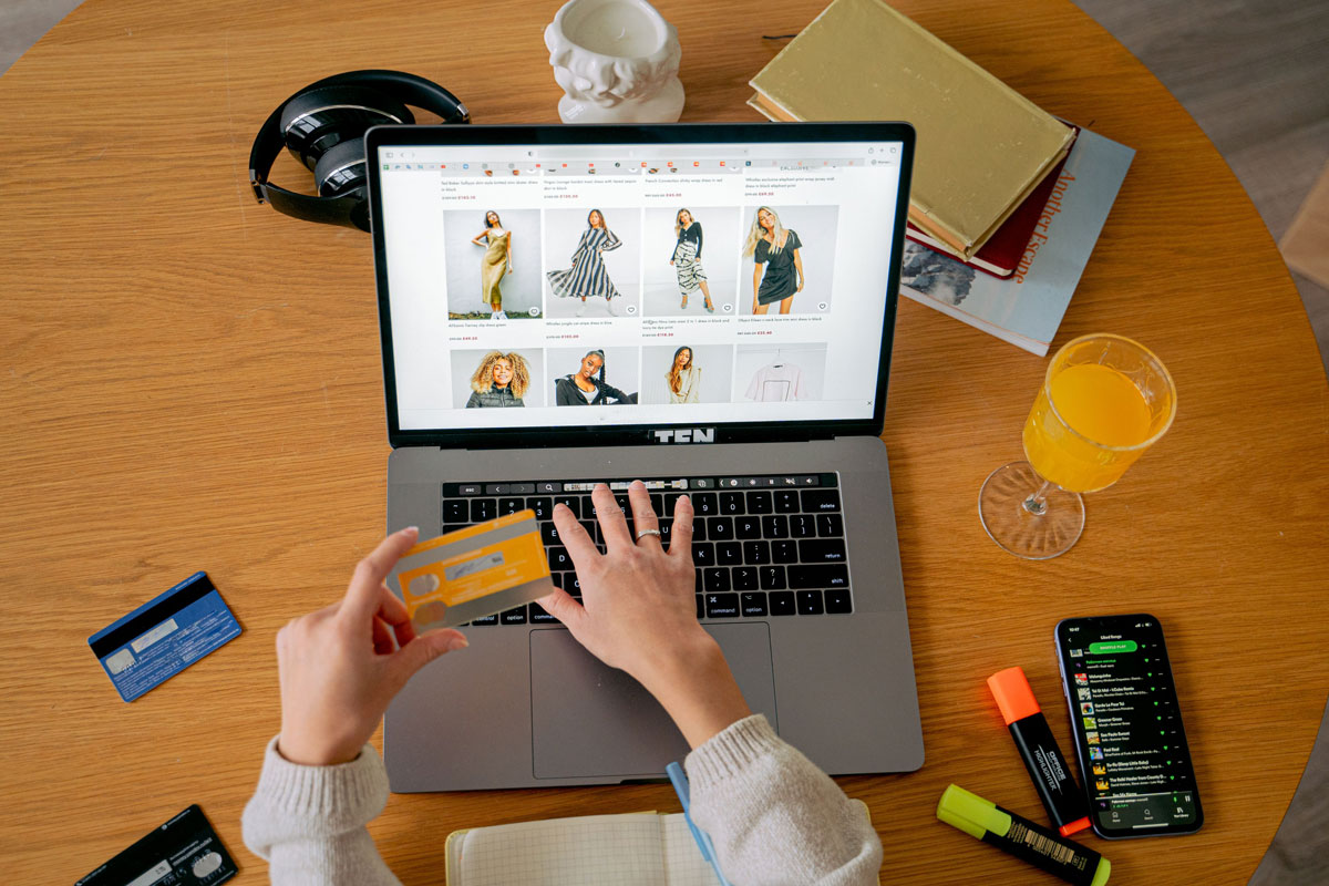Hands holding credit card making online purchase on laptop at wooden desk with various items