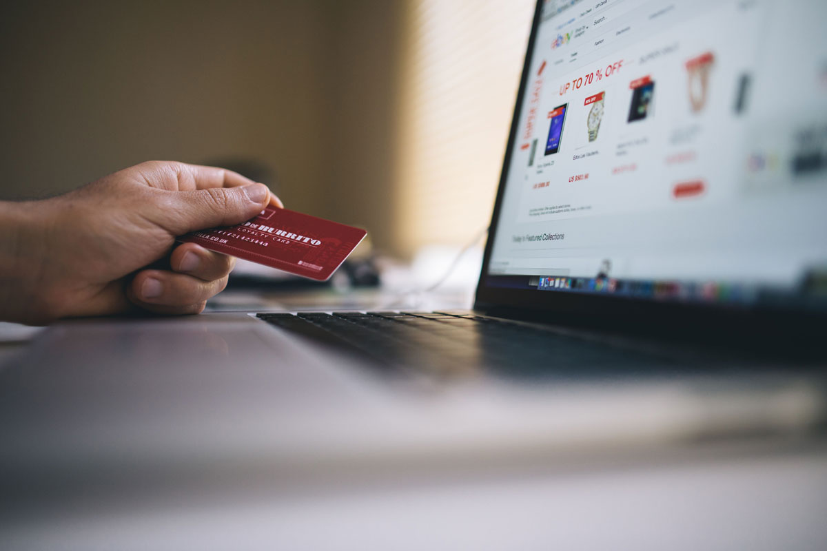 Person holding a credit card while shopping online on a laptop, indicating ecommerce transactions