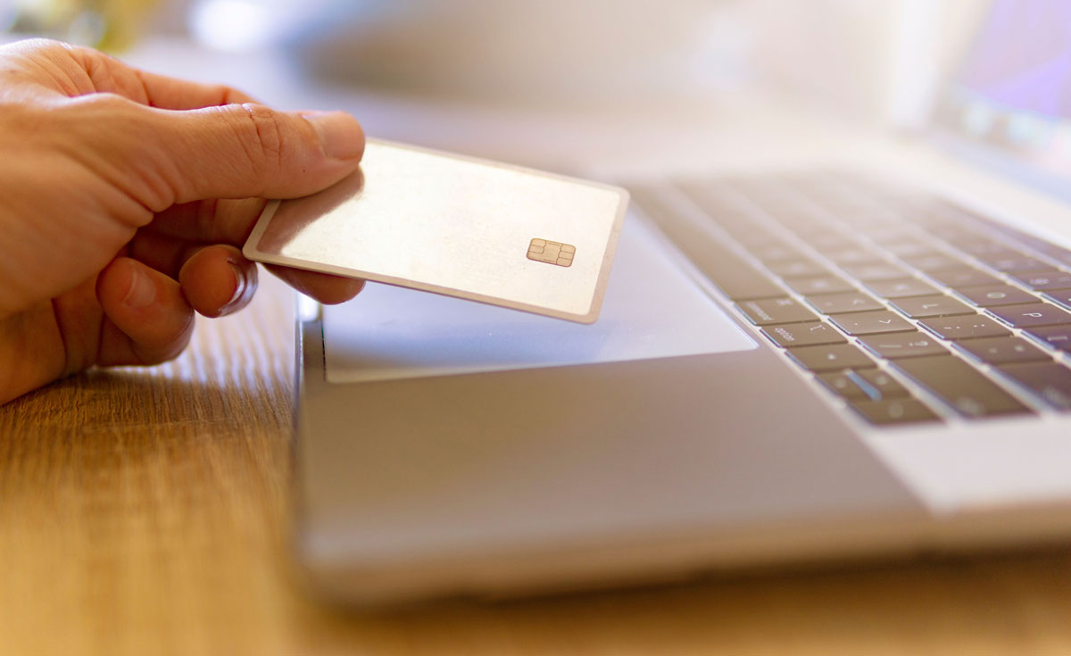 A person holds a credit card near a laptop