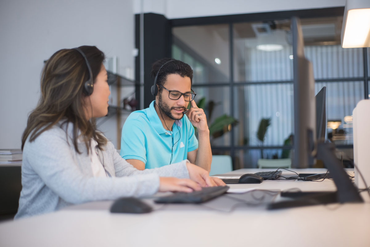 Two call center employees working together in a modern office setting with headsets and computers