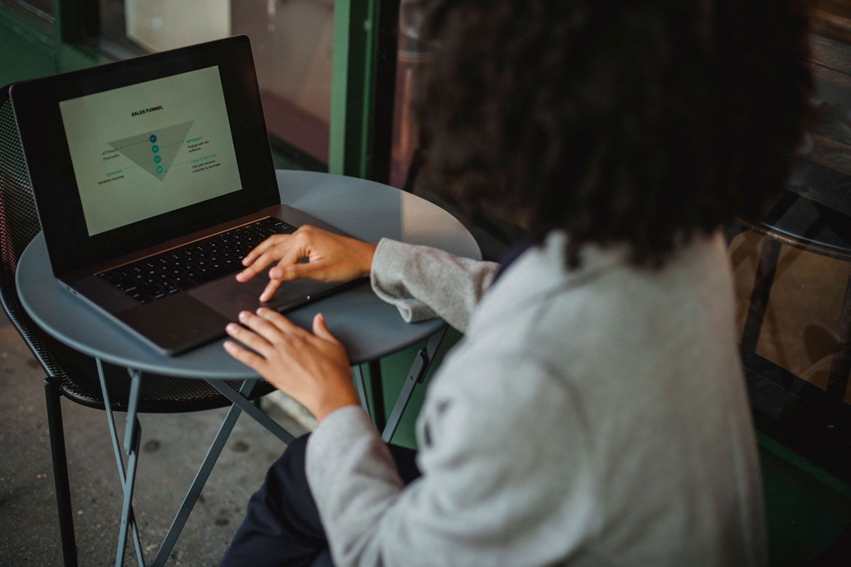 A woman working remotely on a laptop at an outdoor café table, focusing on a sales funnel diagram