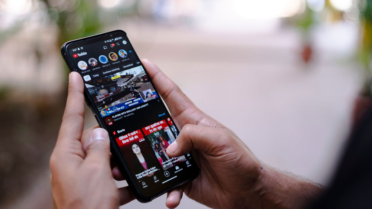 Close-up of hands using a smartphone to watch YouTube outdoors, showcasing digital connectivity