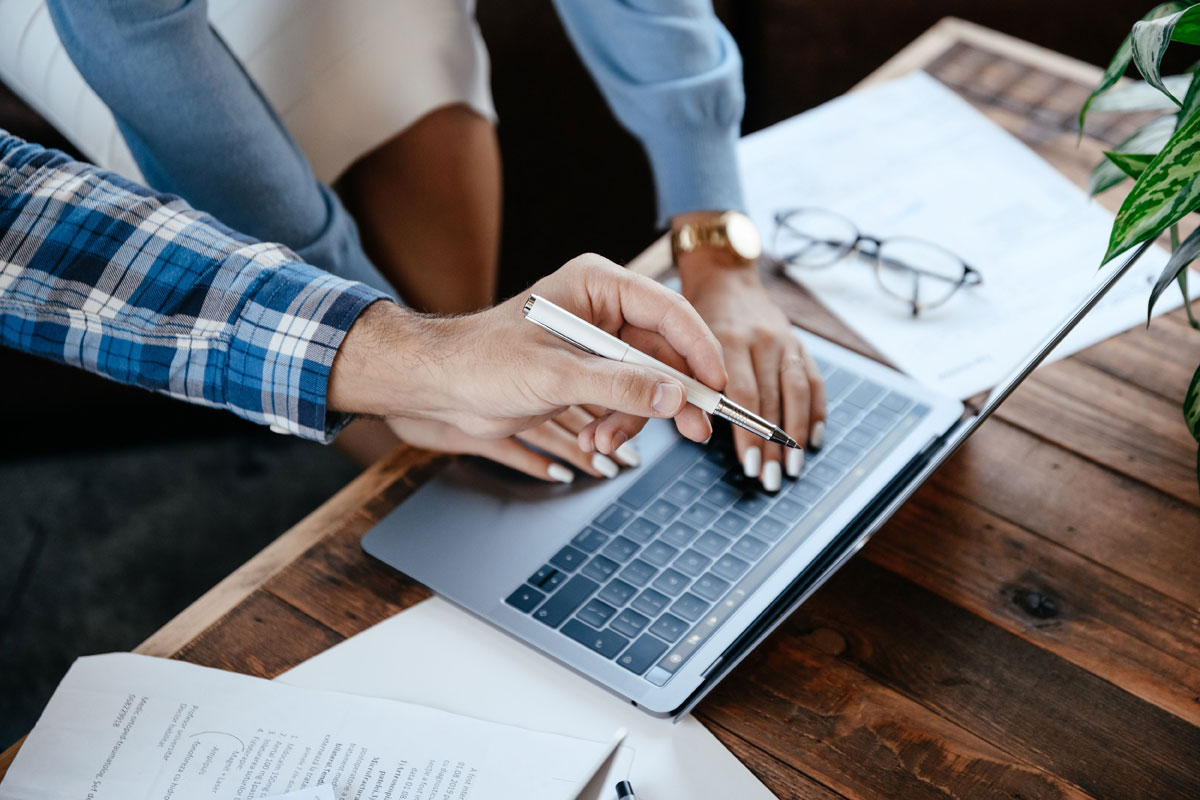 Two professionals collaborating at a wooden desk with a laptop and documents