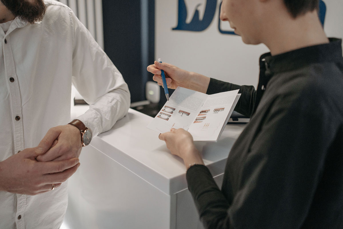Reception staff explaining information to a customer at a clinic counter.