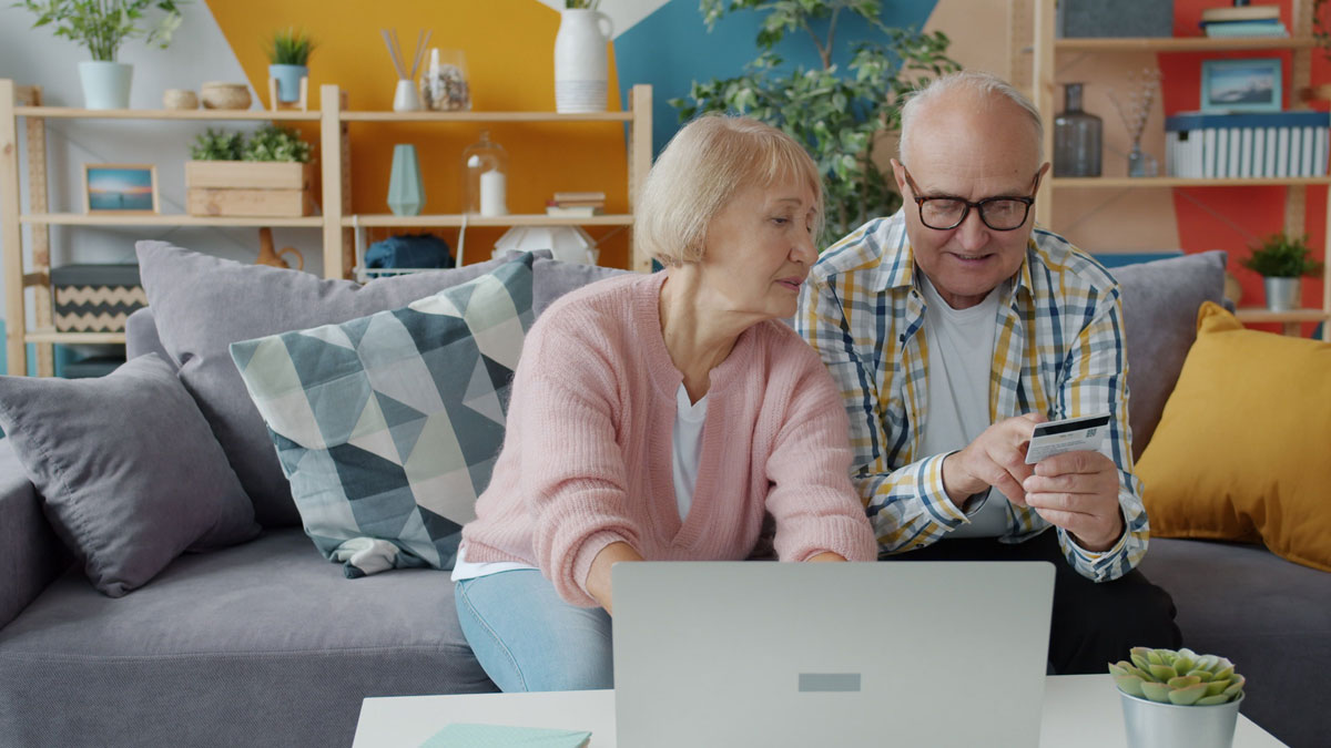 Elderly couple using laptop and credit card in a cozy living room setting.