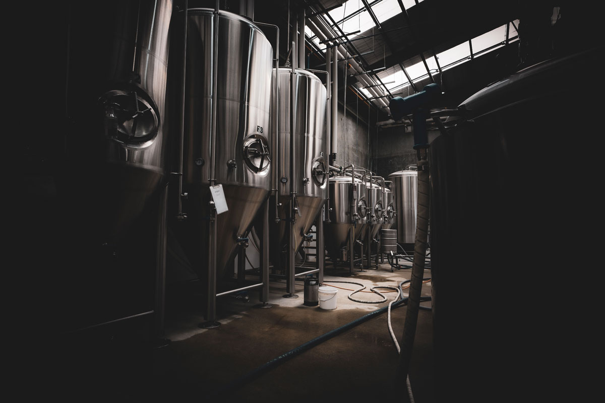 A dramatic interior view of large stainless steel tanks in a dimly lit industrial setting.