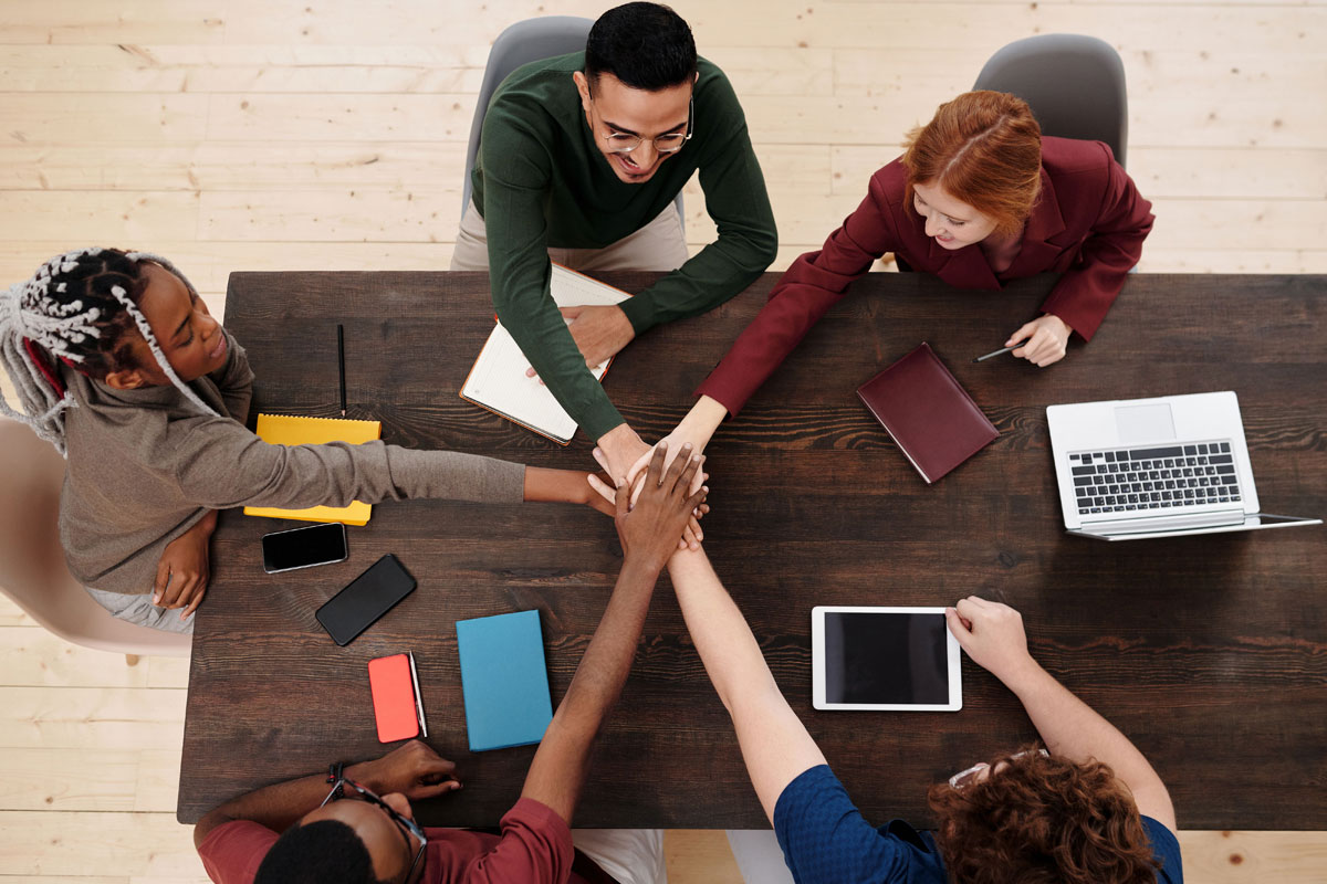 Top view of a diverse team stacking hands in unity over a wooden table, displaying teamwork.