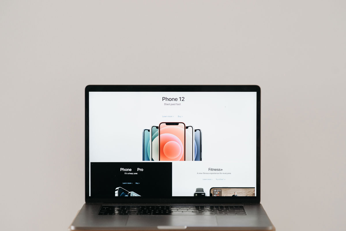 Laptop on stool showing sleek iPhone 12 ad, white background.