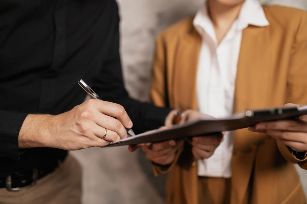 Close-up of two professionals signing a document indoors, focus on hands and pen.