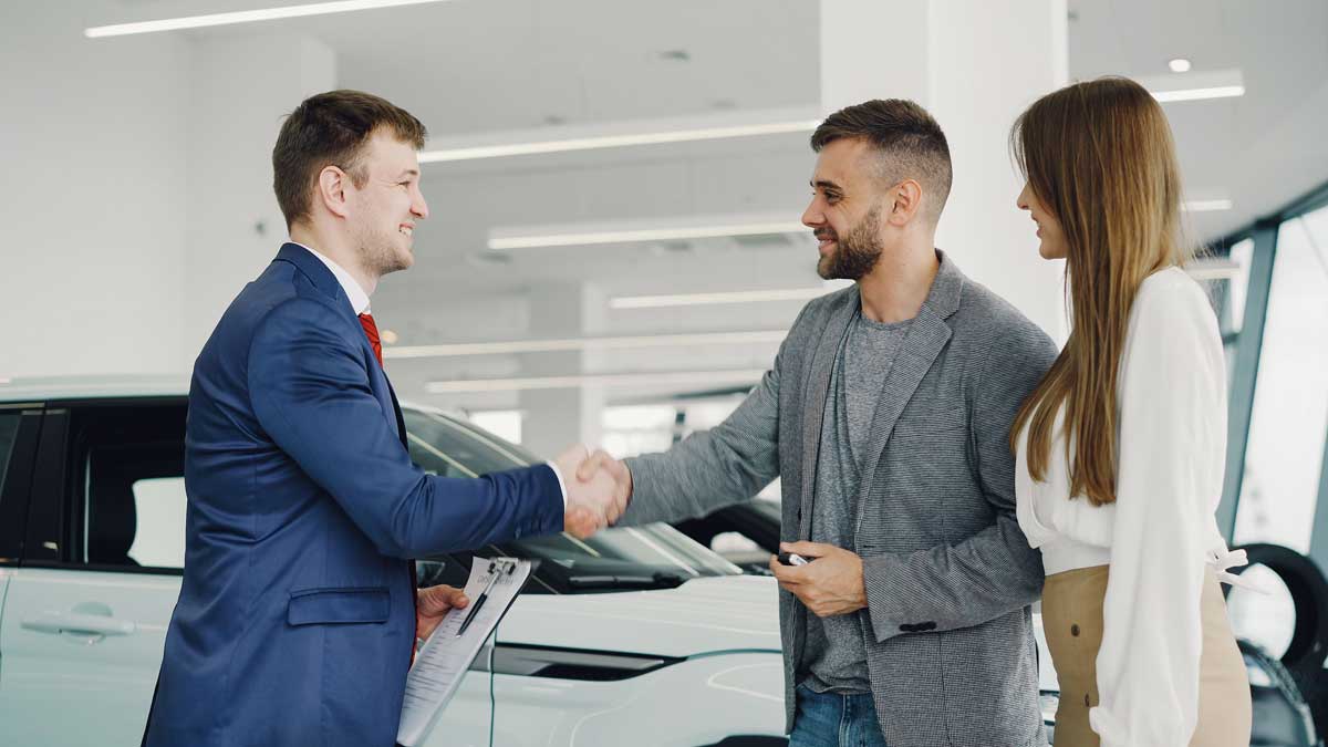 Friendly handshake between a car salesman and customers in a modern car showroom.
