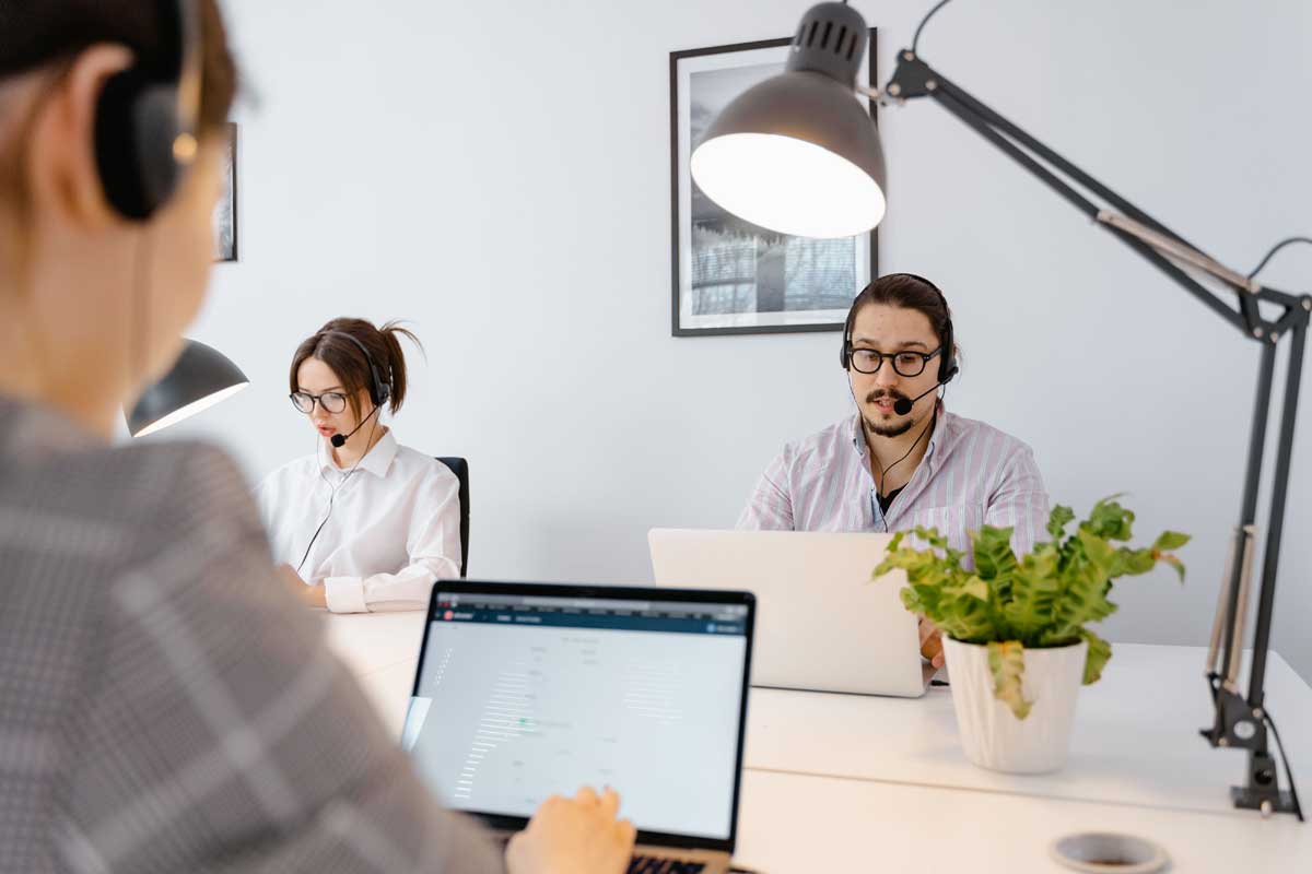 Professional call center agents working on laptops in a bright modern office.